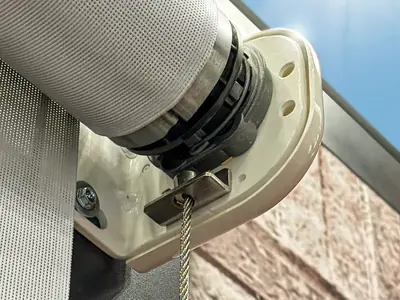 Powder-coated aluminum roller tube end bracket with an internal stainless-steel cable guide for a Solair® Vertical Cable Curtain, shown in bright sunlight