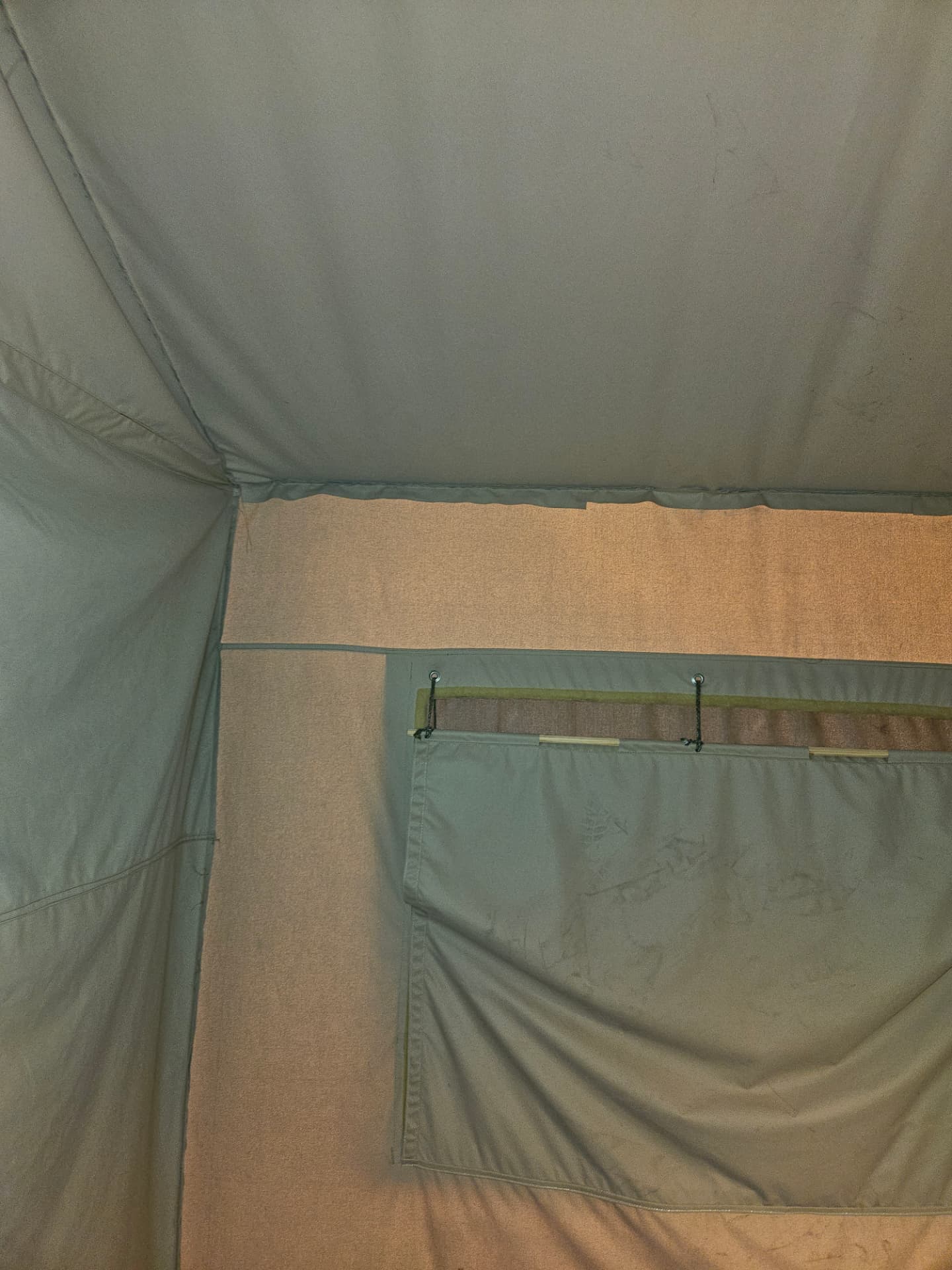 Interior of a canvas safari glamping tent showing the sewn roof seam, ridge, and a rolled canvas window flap with tie chains during a glamping tent repair