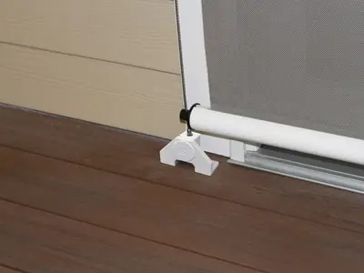 White horizontal bottom bar of a Solair® Vertical Cable Curtain resting in a plastic cable foot anchored to a wooden deck, with a vertical stainless-steel guide cable