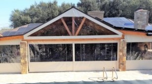 Manual roll-up outdoor curtains on a San Antonio area patio with wood header and stone columns — beige fabric panels rolled down to block sun and neighbors while keeping the outdoor view