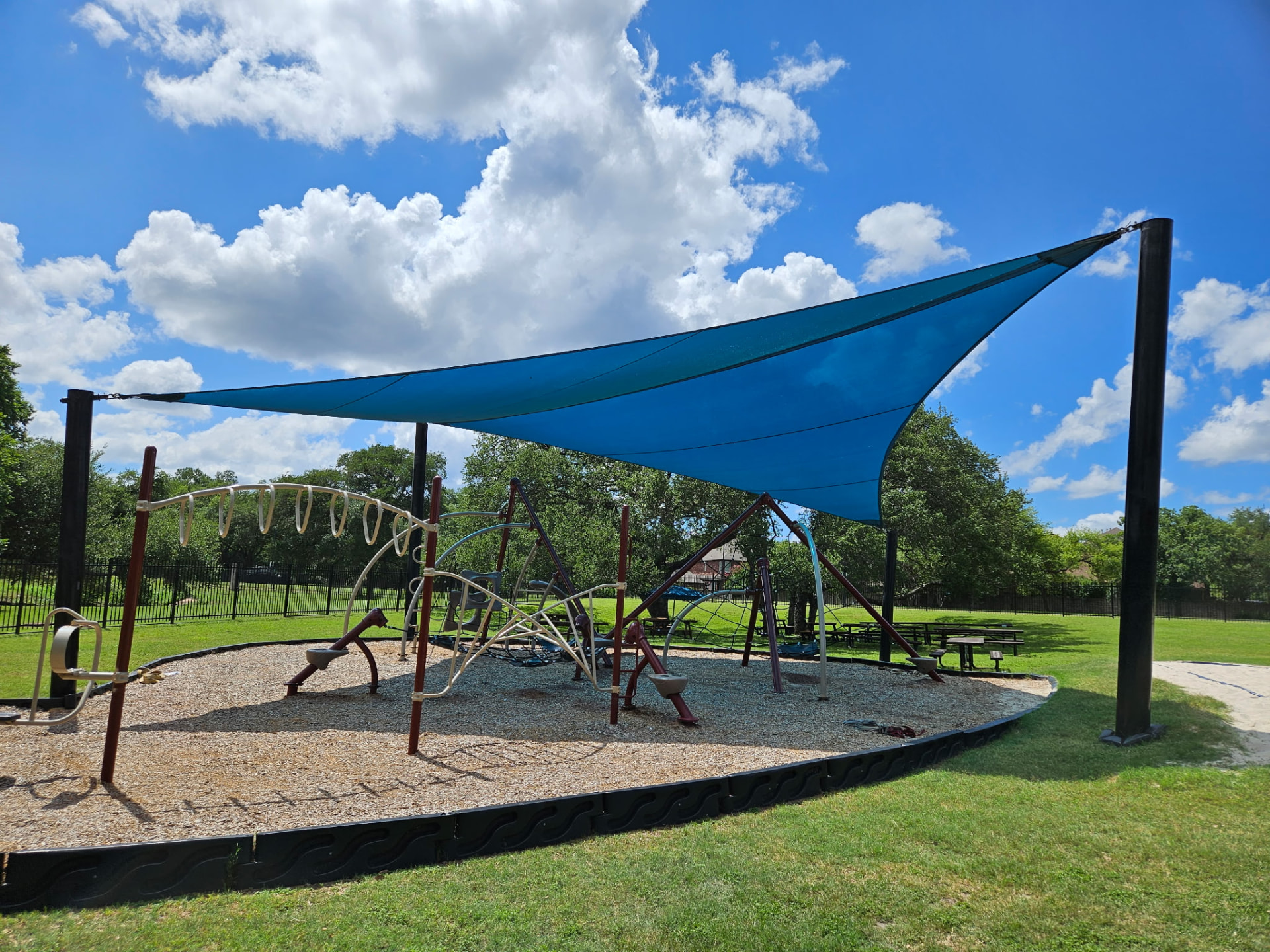 Teal tensioned shade sail over a neighborhood playground in Austin, Texas — custom sail shade tension structure by Texas Made Shade