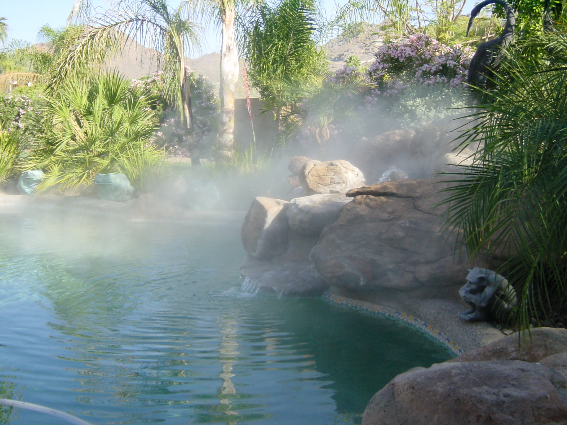 Poolside fogging system filling a rock waterfall and palm landscape with cool mist