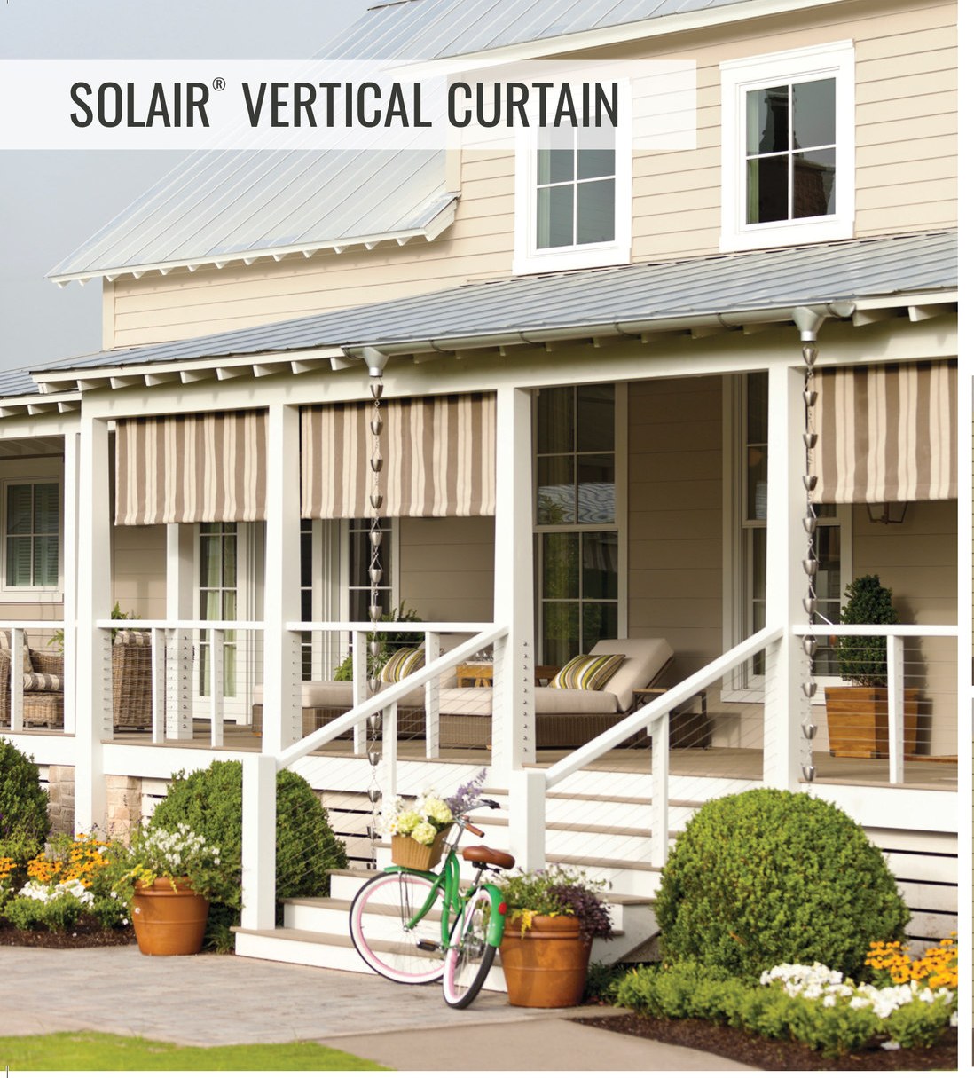 Two Solair® Vertical Curtains in tan and cream stripe lowered between the posts of a covered farmhouse porch with rocking chairs