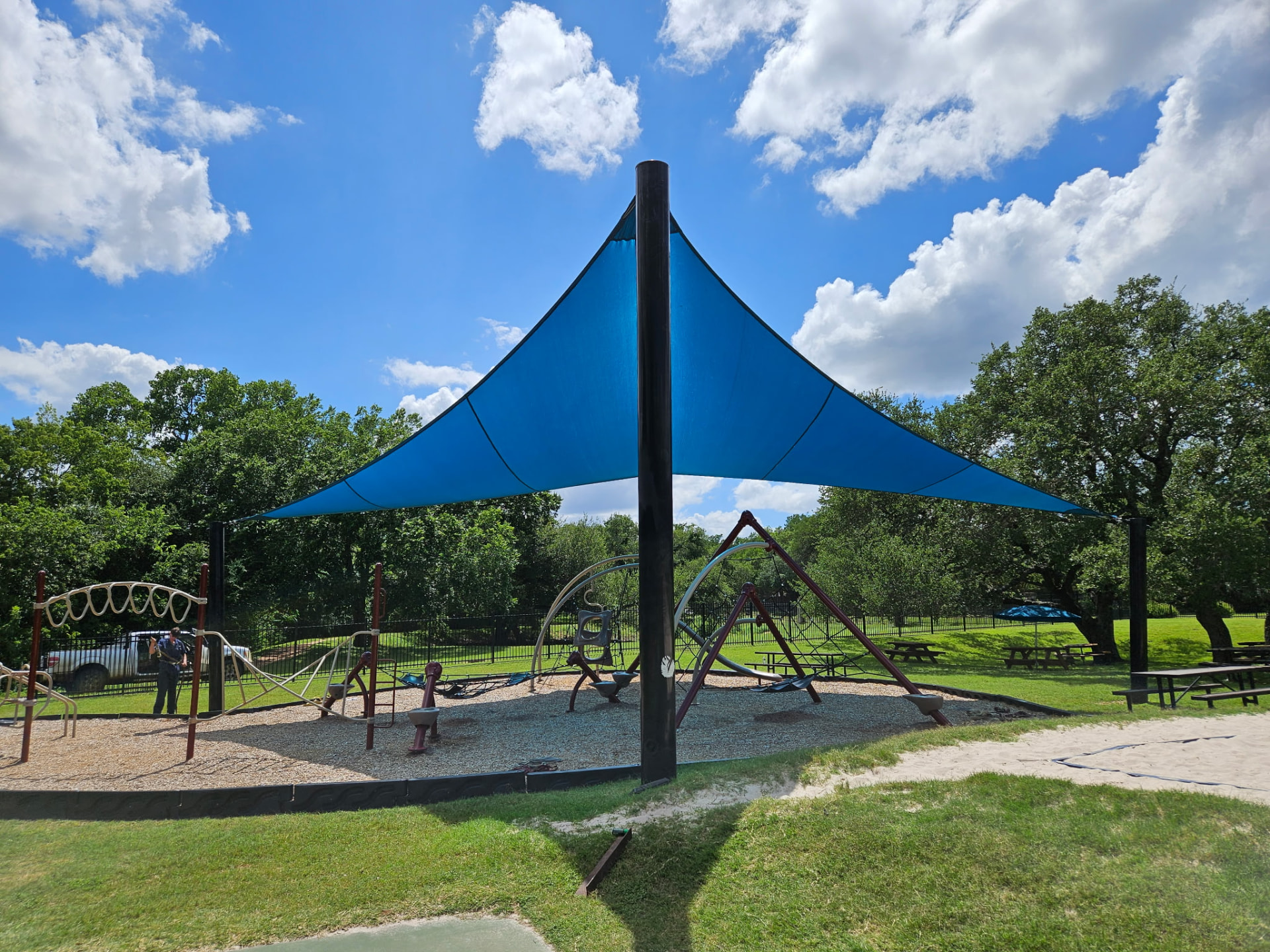 Center-post hypar tension shade sail over playground equipment in Austin, Texas — twisted-geometry shade sail structure