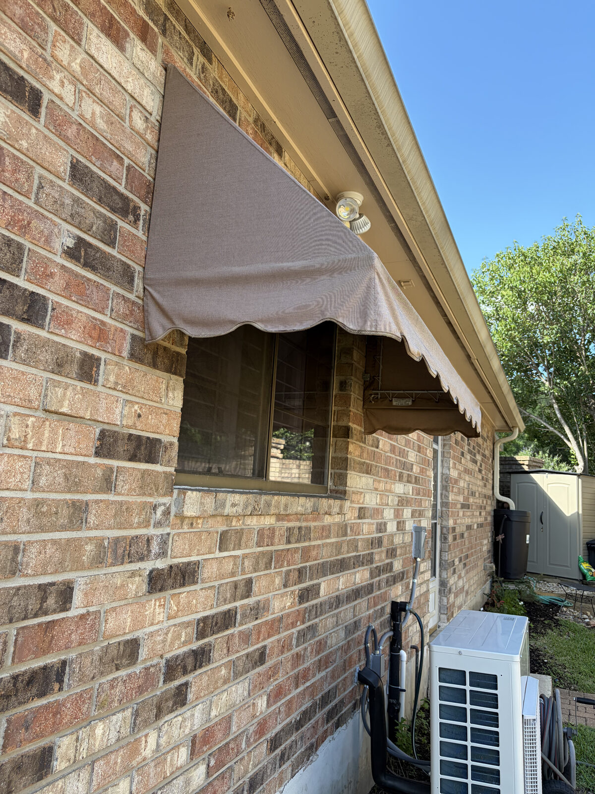 Home Awning — custom residential window awning in mocha canvas over a brick home, fabricated and installed by Texas Made Shade
