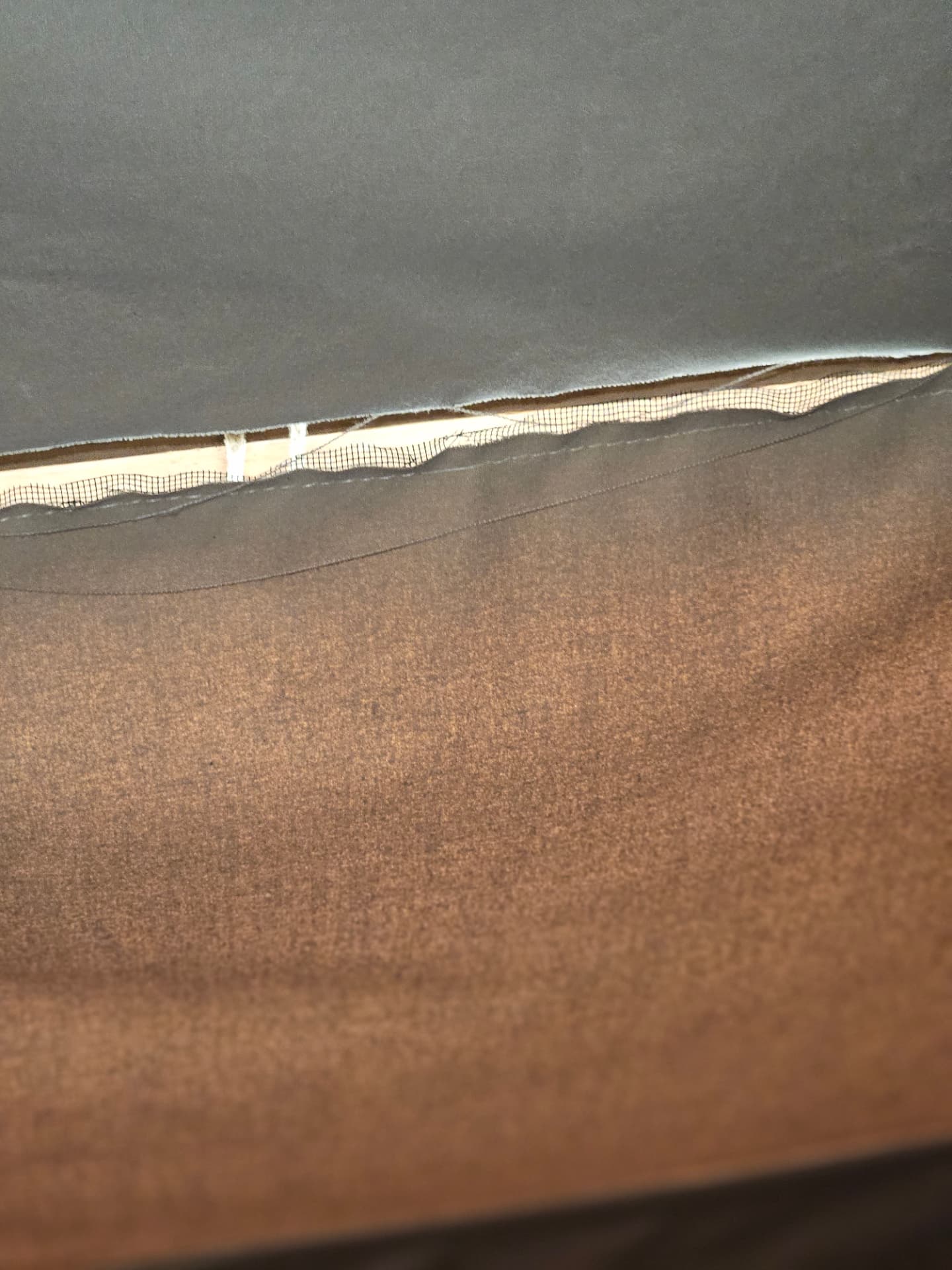 Open seam and torn canvas along a glamping tent roof edge, showing the mesh backing and stitching that has to be re-sewn during a tent repair