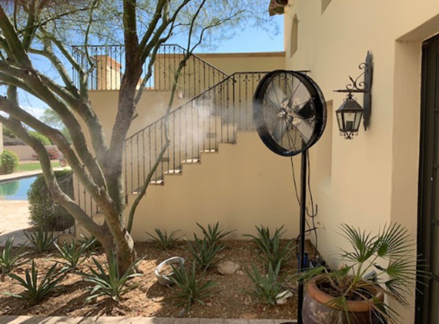 Portable oscillating pedestal misting fan spraying fine mist across a residential courtyard patio