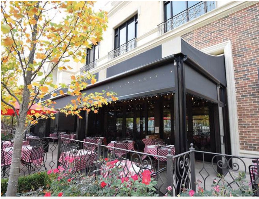 Solair® Power Screens enclosing a restaurant patio with a red awning above the bar seating