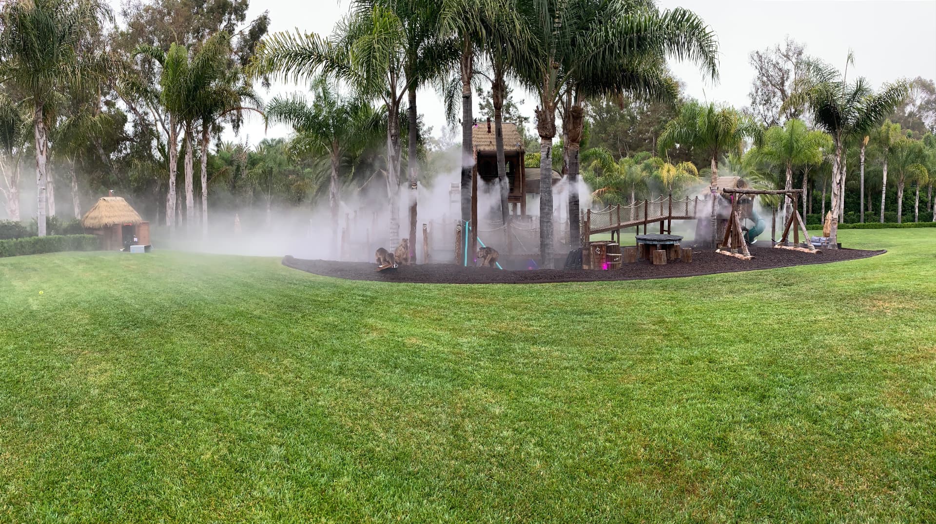 Backyard playground surrounded by a wall of cooling fog from an outdoor misting system