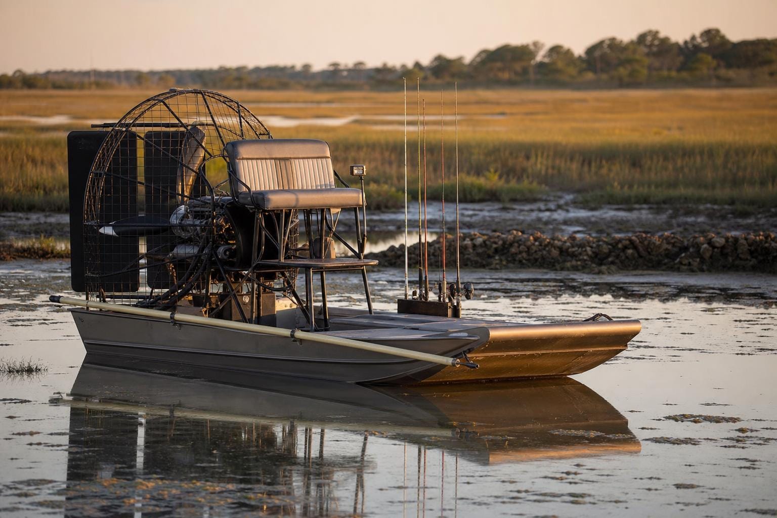 Texas fishing-guide air boat with low-profile aluminum hull, rear fan cage, raised guide platform and rod holders on a coastal marsh at golden hour