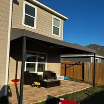 Custom back porch retractable awning in Sunbrella® Smoke fabric shading a stained concrete patio on a Texas ranch-style home