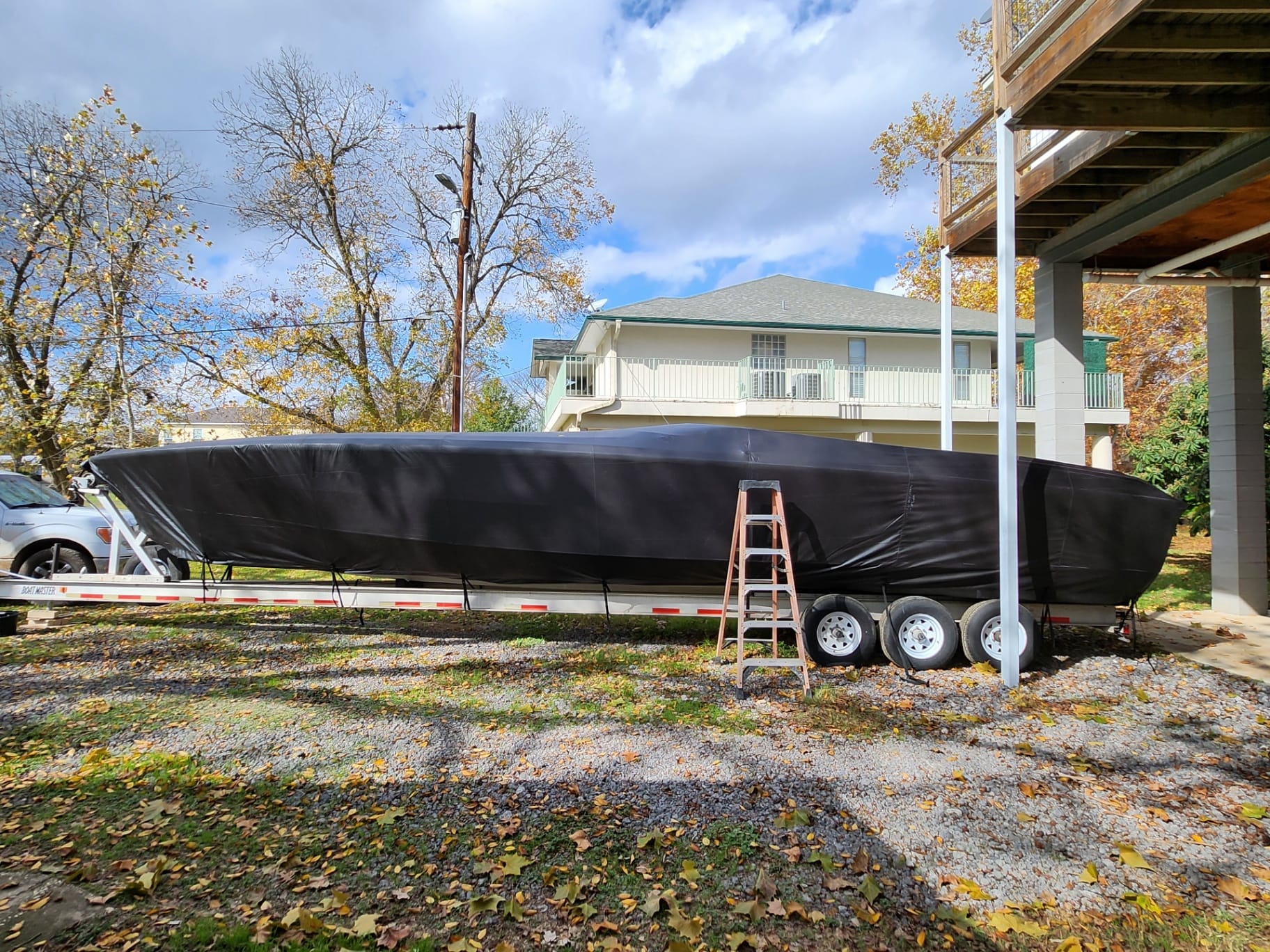 Custom black heavy-duty marine canvas full storage cover fabricated by Texas Made Shade, fitted snug over a large offshore performance boat on a triple-axle trailer at a Central Texas lakehouse