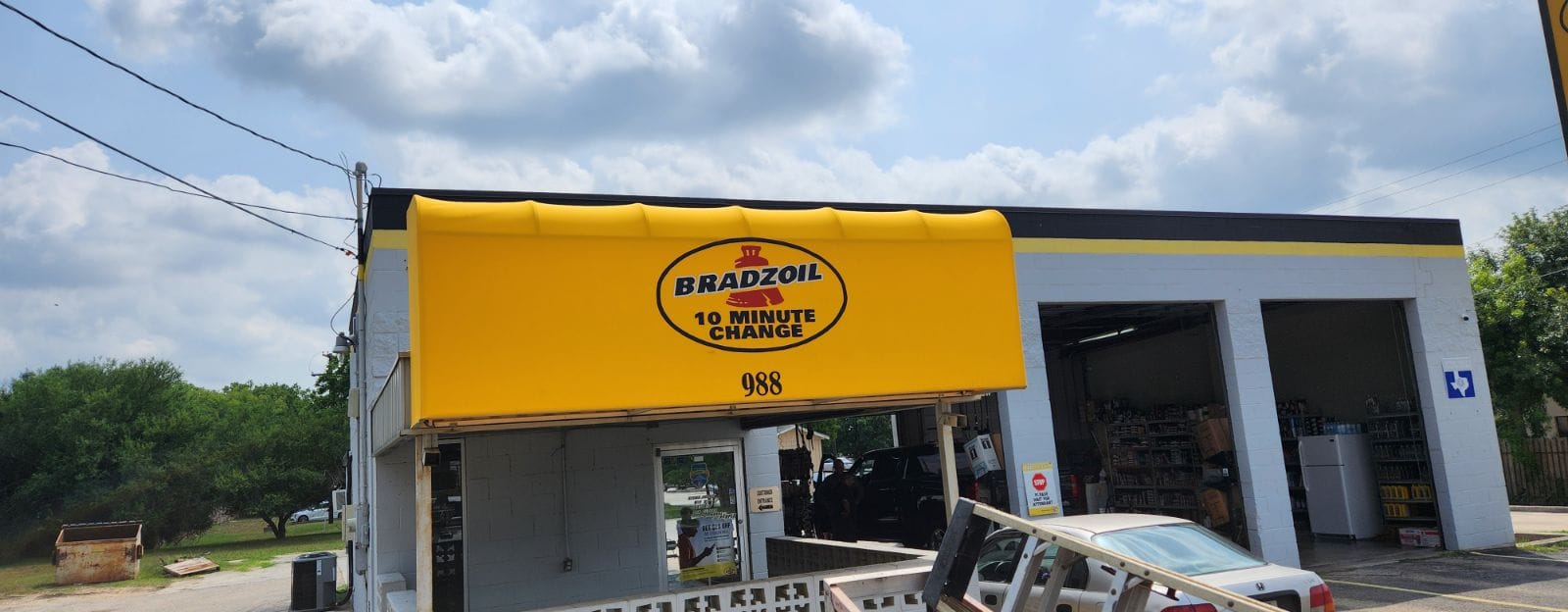 Custom bright yellow Sunbrella canvas canopy awning fabricated and installed by Texas Made Shade for Bradzoil 10 Minute Oil Change — welded aluminum frame with branded commercial canopy over the storefront entrance