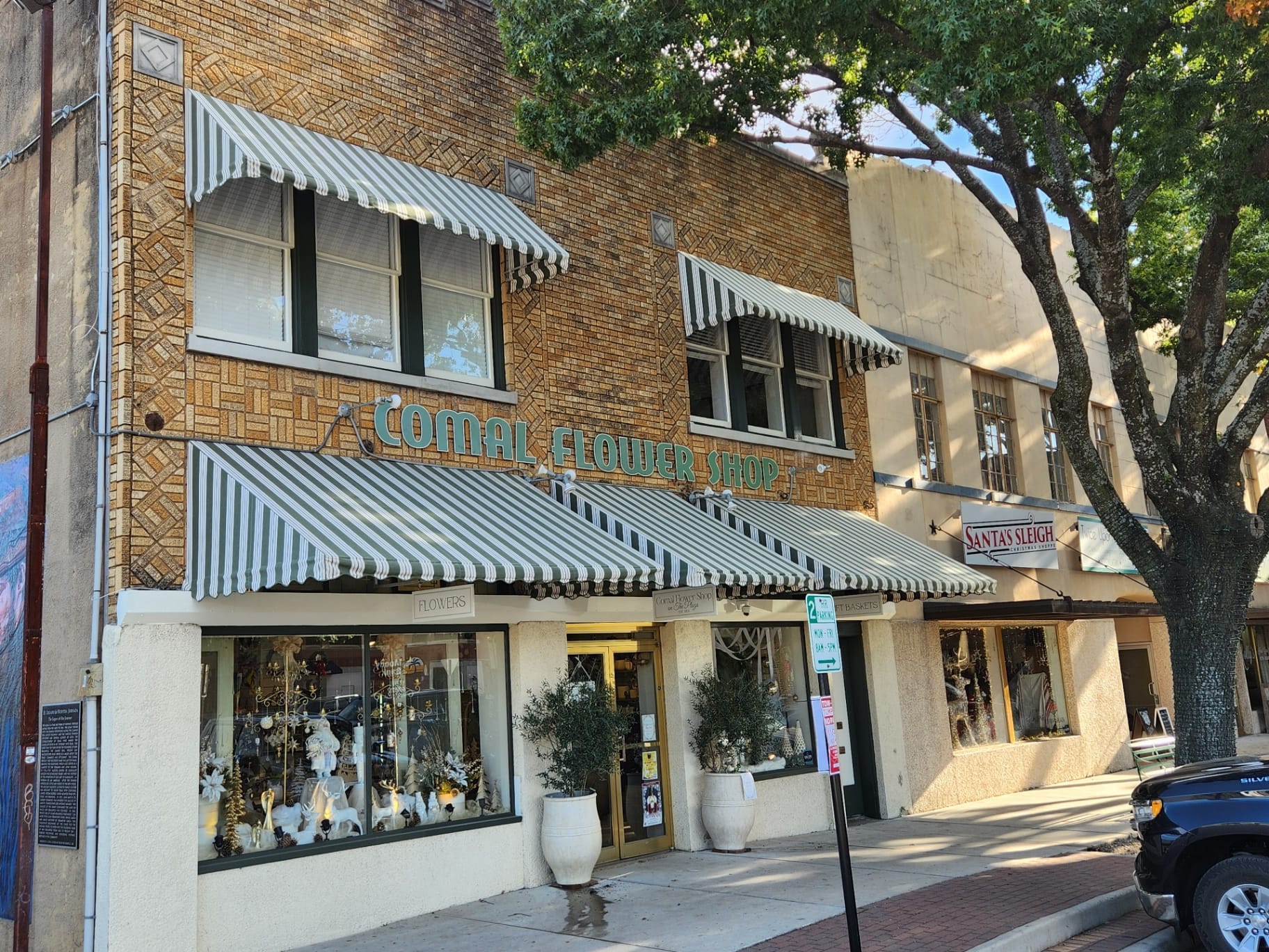 Set of green-and-cream striped Sunbrella storefront and window awnings installed by Texas Made Shade over Comal Flower Shop in downtown New Braunfels