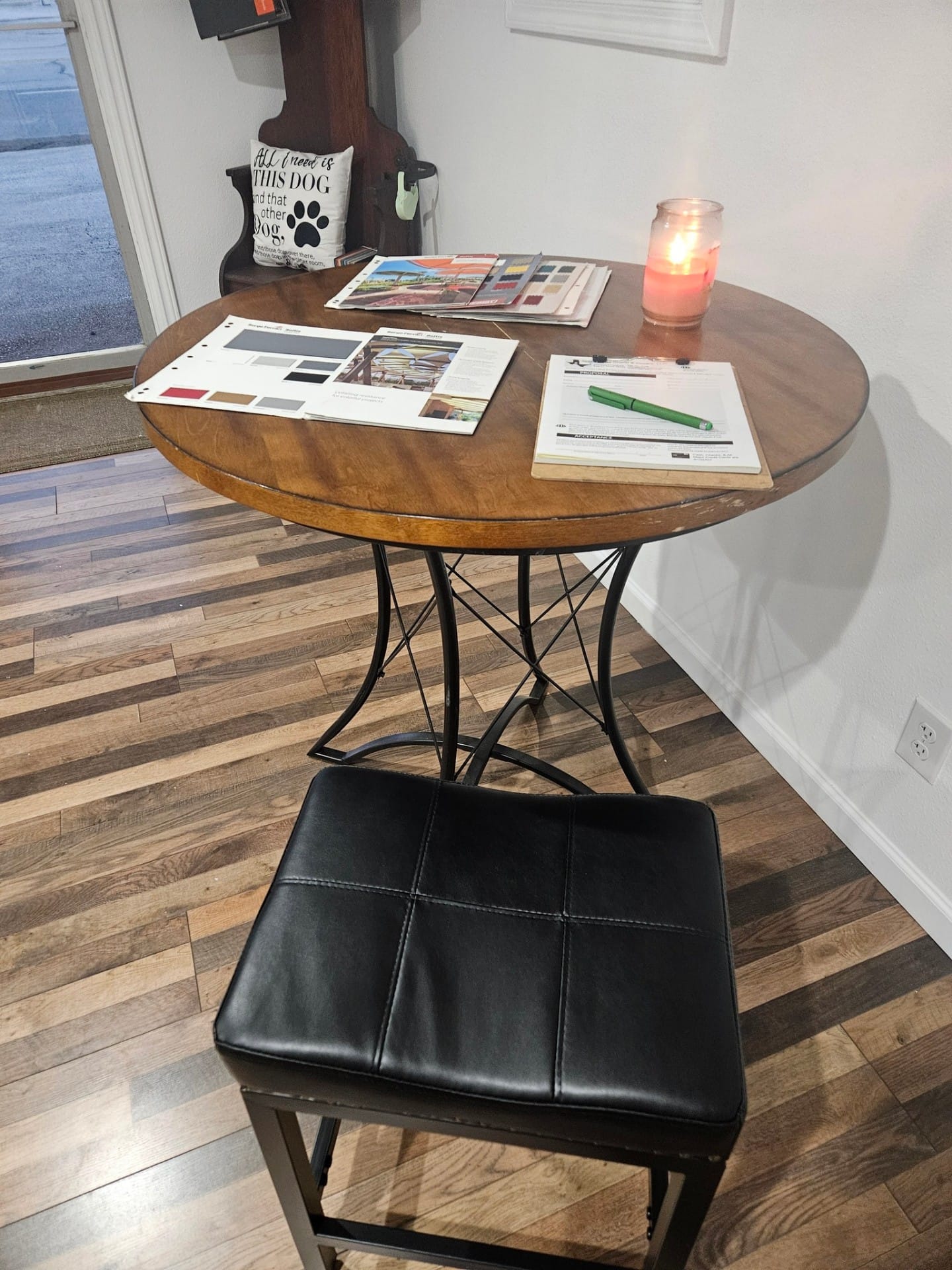 Customer consultation table inside the Texas Made Shade & Covers Seguin showroom — Sunbrella and Serge Ferrari fabric sample books, a written proposal, and a candle laid out on a round wood-top table with a leather barstool
