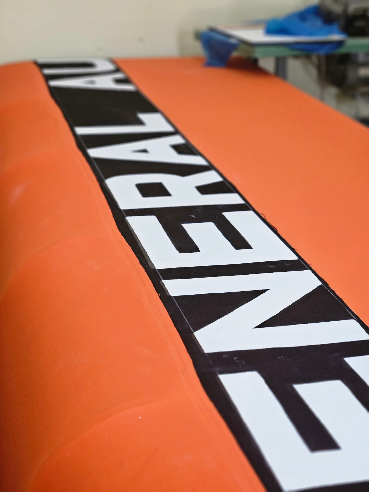 Close-up of crisp hand-painted white block letters on a black band across a bright orange Sunbrella commercial canopy in the Texas Made Shade Seguin shop