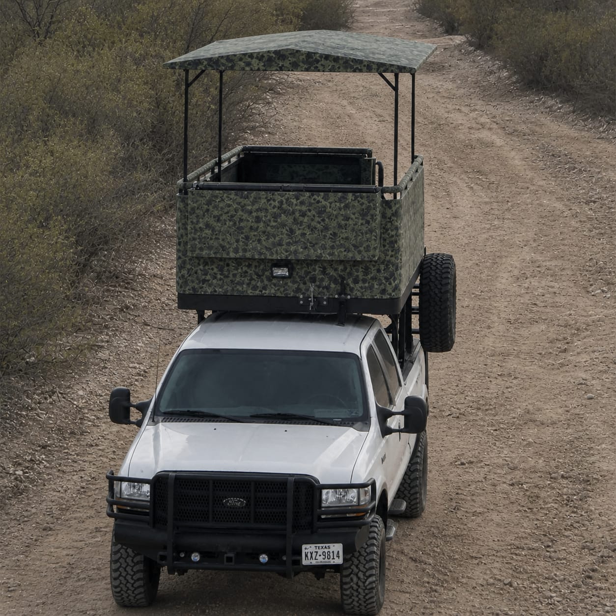 Lifted Ford truck on a South Texas brush-country sendero with a custom camo high-rack hunting blind — camo canvas wrap and roof patterned and sewn by Texas Made Shade