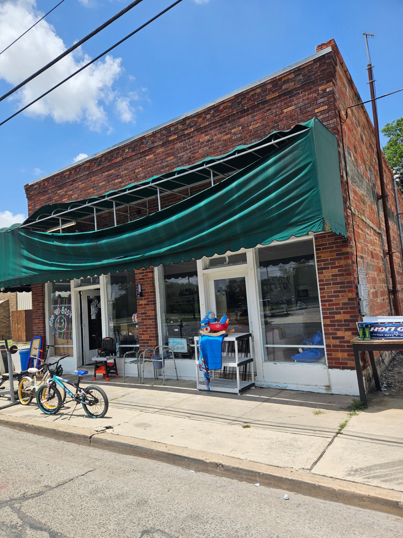 Faded and sagging green canvas storefront awning on a brick building in San Antonio, TX — existing welded aluminum frame is sound and ready for a recover by Texas Made Shade