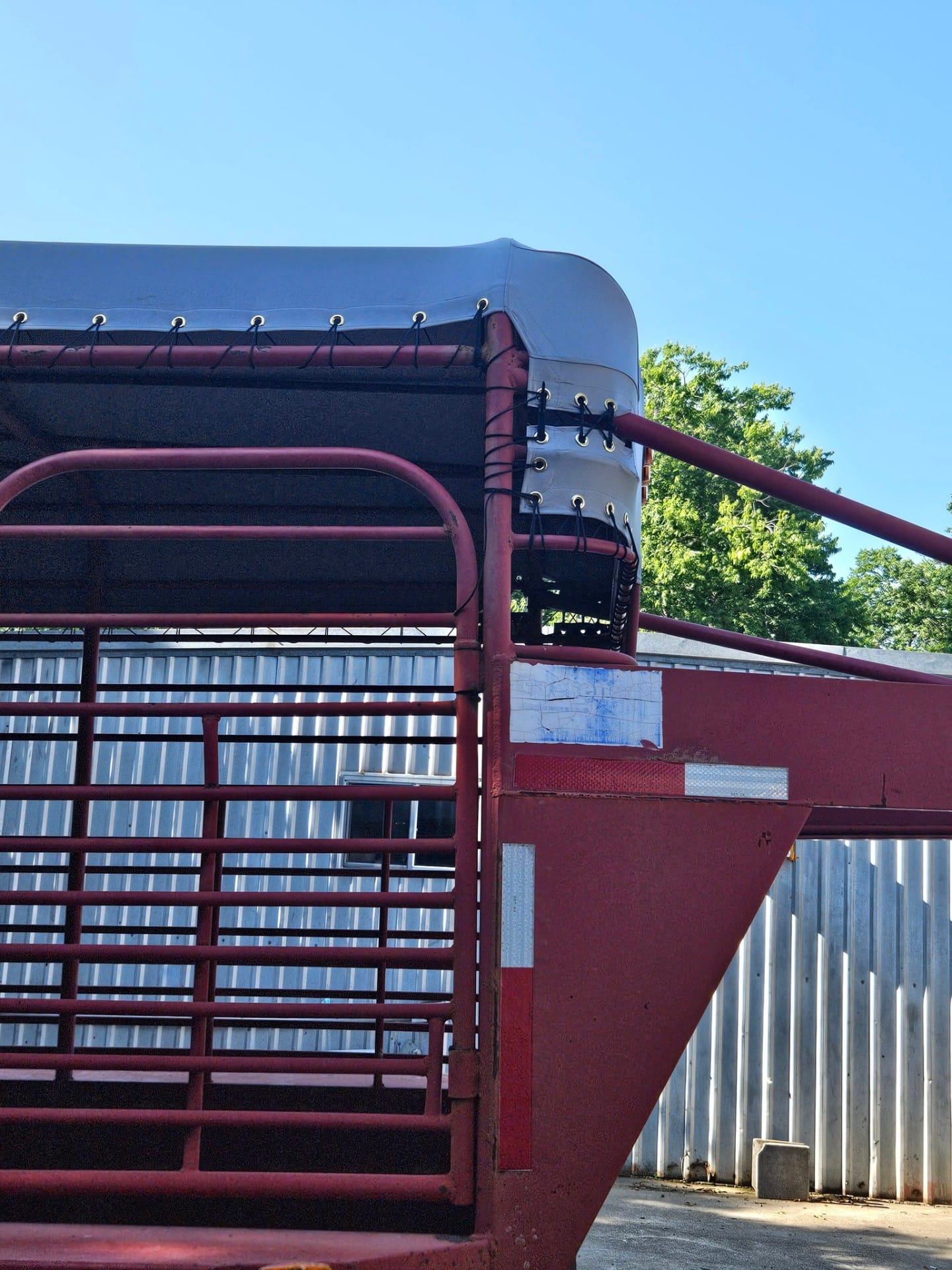 Close-up of the front gooseneck corner on a red stock trailer showing a custom gray vinyl top laced down through brass grommets with shock cord