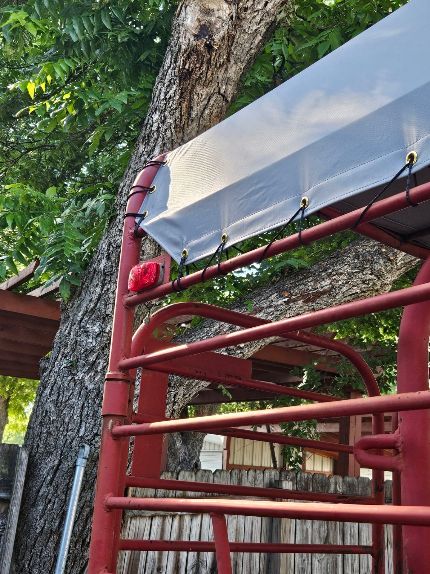 Detail of the rear corner of a red gooseneck stock trailer cover showing reinforced gray vinyl edge, brass grommets, and black shock-cord lacing tied to the top rail