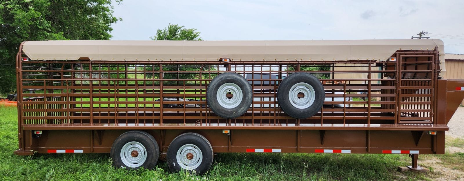 Brown long-bed gooseneck cattle trailer with two spare tires, fitted with a tan heavy-duty vinyl top cover patterned by Texas Made Shade