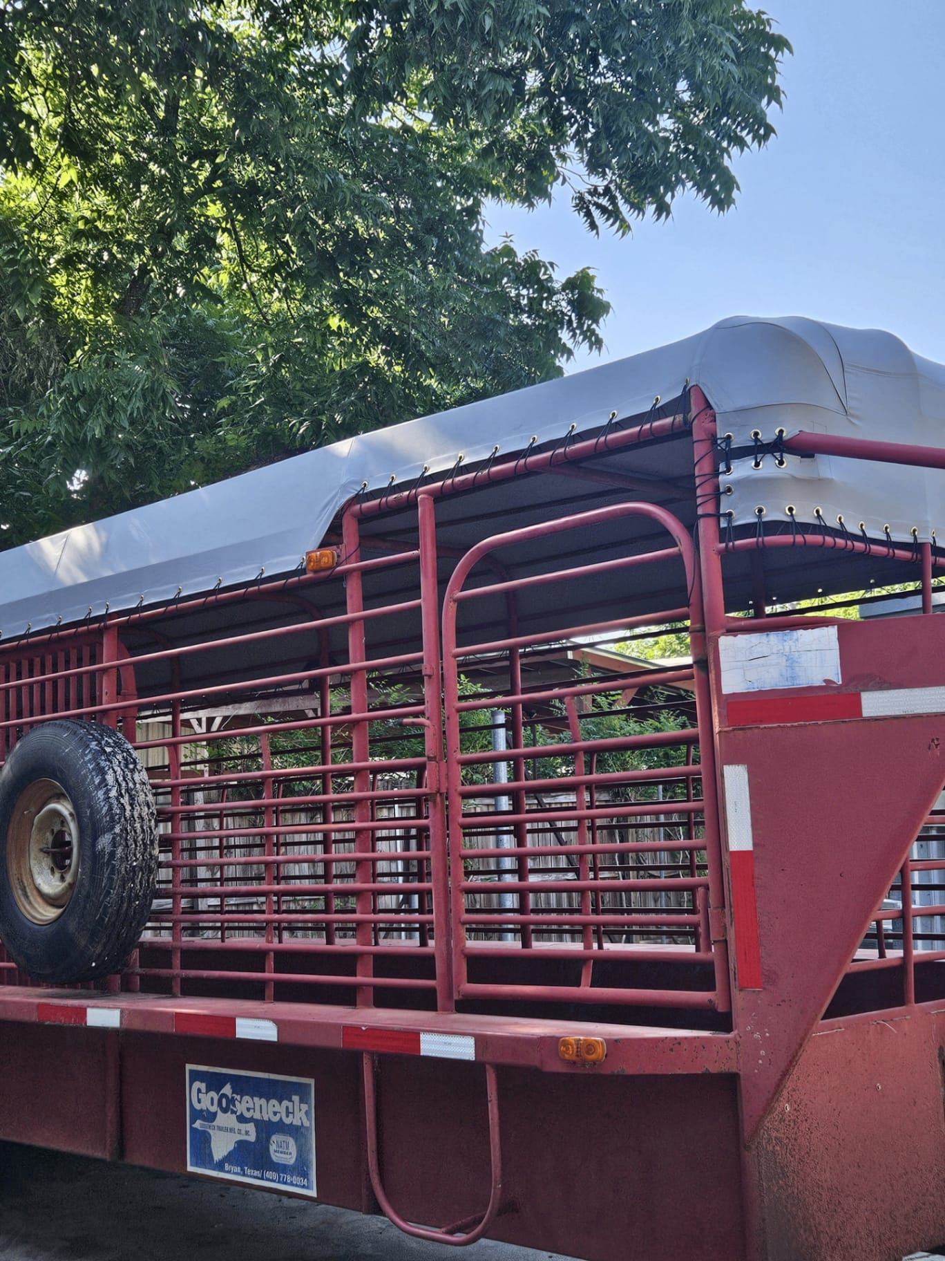 Installed custom-fit white 18oz vinyl top cover stretched tight over the rails of a red gooseneck cattle trailer for a Central Texas ranch