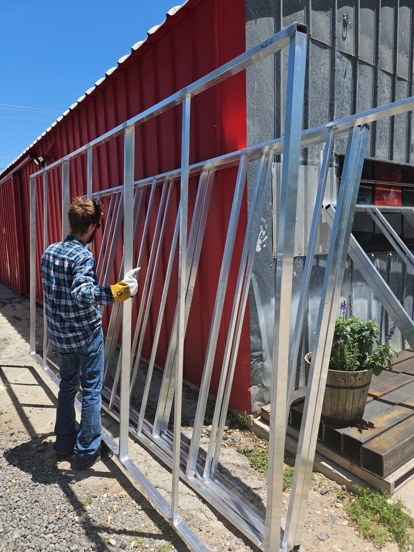 Texas Made Shade fabricator standing a fully welded structural aluminum awning frame upright against the Seguin shop wall, showing the full lattice of vertical members, diagonal braces, and horizontal rails after final TIG welding